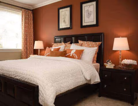 Well-decorated bedroom with a large bed, nightstands and lamps against a burnt-orange accent wall.