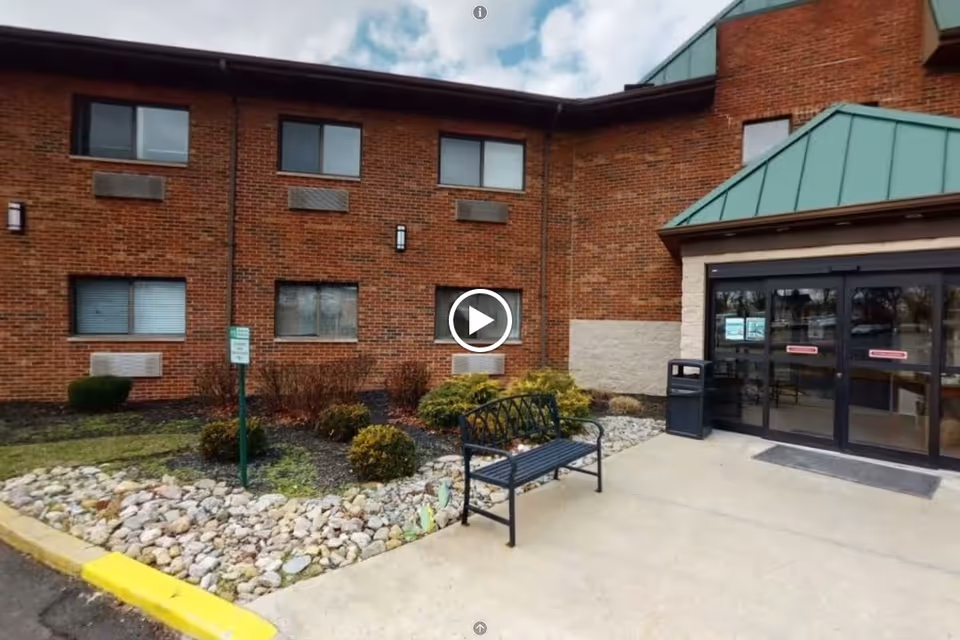 Entrance of a brick senior living building with a bench, landscaped rock bed, and automatic glass doors.