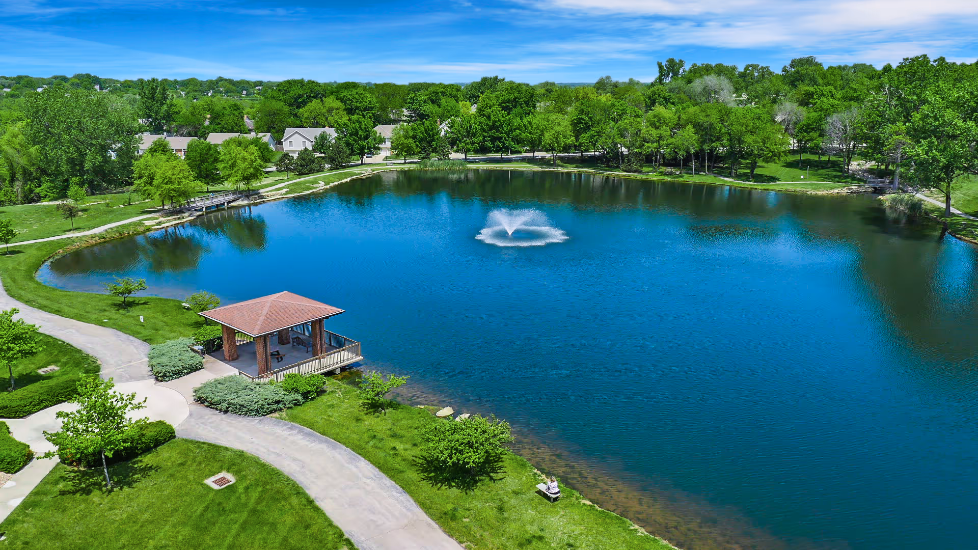 Aerial view of a pond with a central fountain, a gazebo on the shore, walking paths and surrounding trees at Lakeview Village.