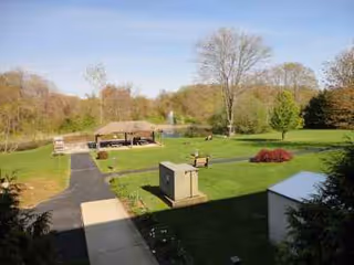 Well kept outdoor lawn with gazebo, benches, and a paved walkway at a senior living campus.
