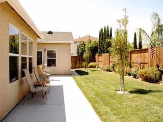 Outdoor patio beside a beige building with seating, a grassy yard, and a wooden fence.