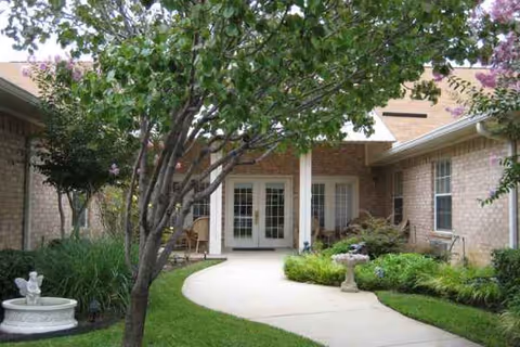 Front entrance of a brick senior living facility with a curved walkway and landscaped garden.
