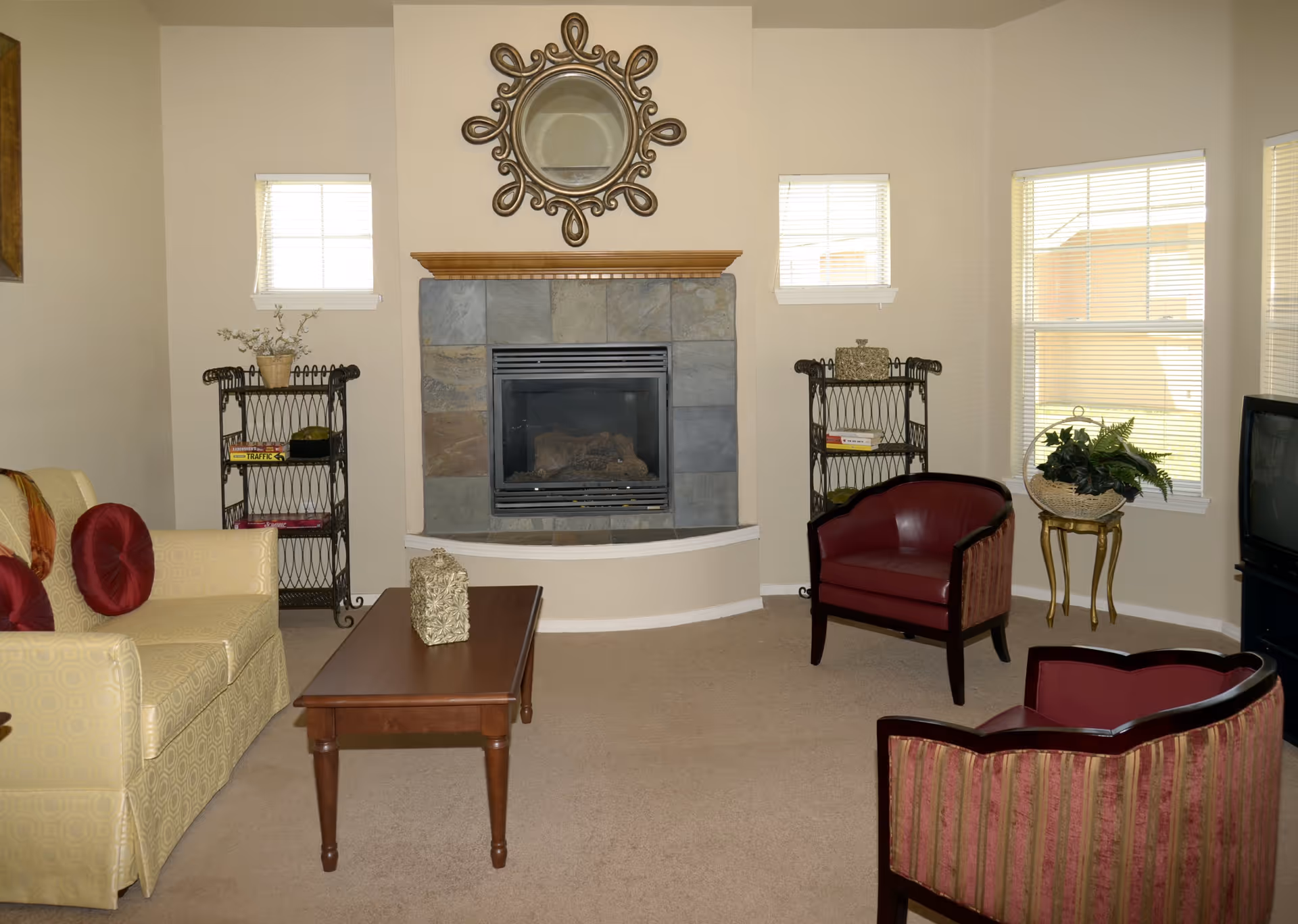 A cozy living room with a central fireplace topped by a decorative mirror, a sofa and armchairs around a coffee table, and multiple windows.