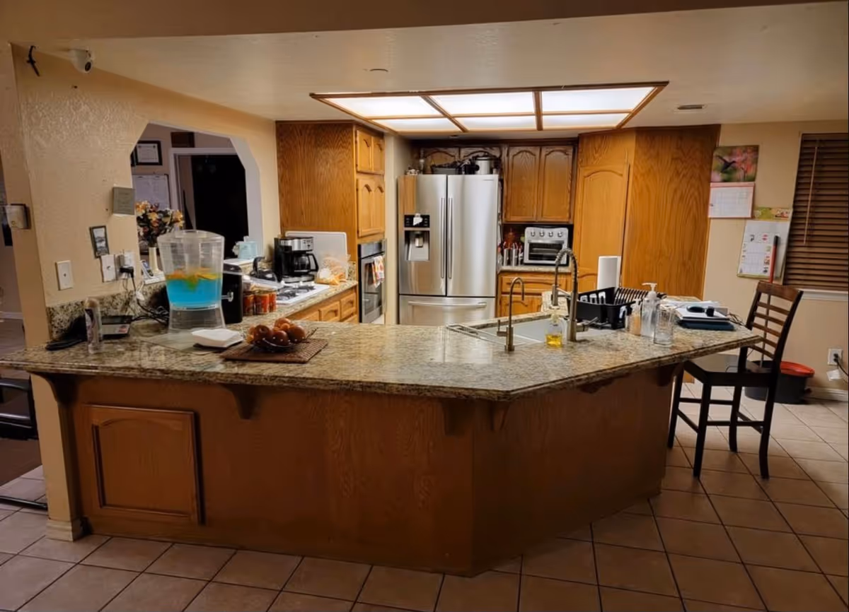 Senior living facility kitchen with granite island, stainless appliances, and wooden cabinets.