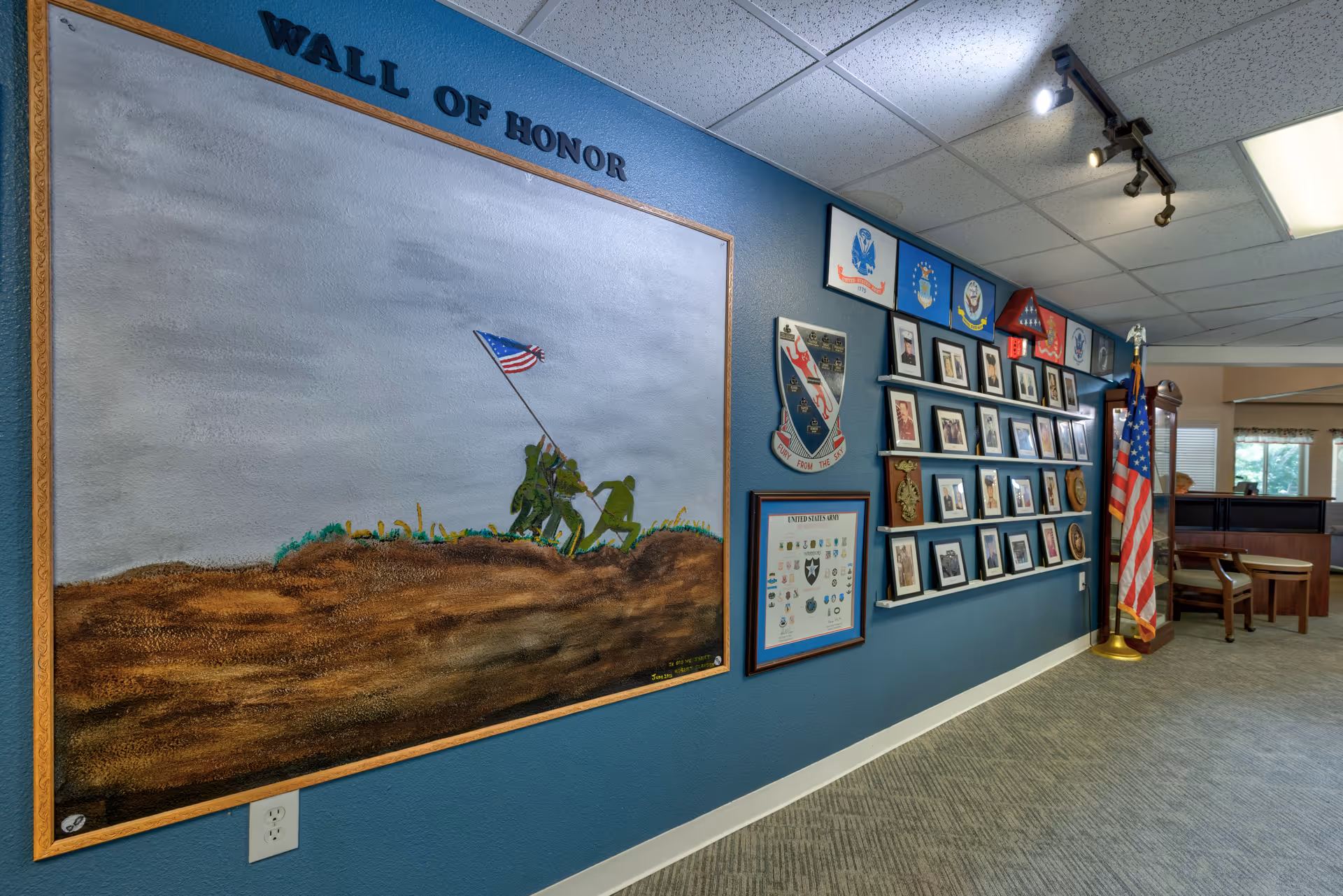 Interior hallway showing a 'Wall of Honor' display with a mural, framed photos and plaques, and an American flag.