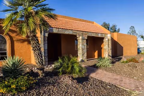 Sunrise Care Home Shea exterior with orange stucco walls, stone columns, and desert landscaping.