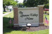 Brick-framed lawn sign reading 'The Lebanon Valley Home' with small American flags on each side.