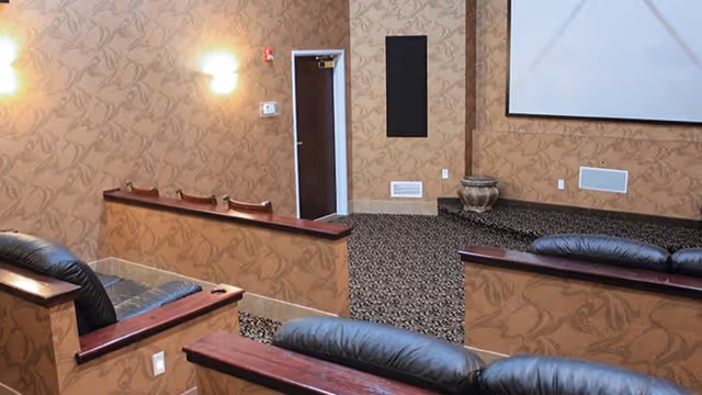Small theater-style screening room with tiered leather seating, patterned wallpaper, and a projection screen.