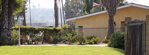 Exterior view of a yellow senior living facility with a lawn and gate.