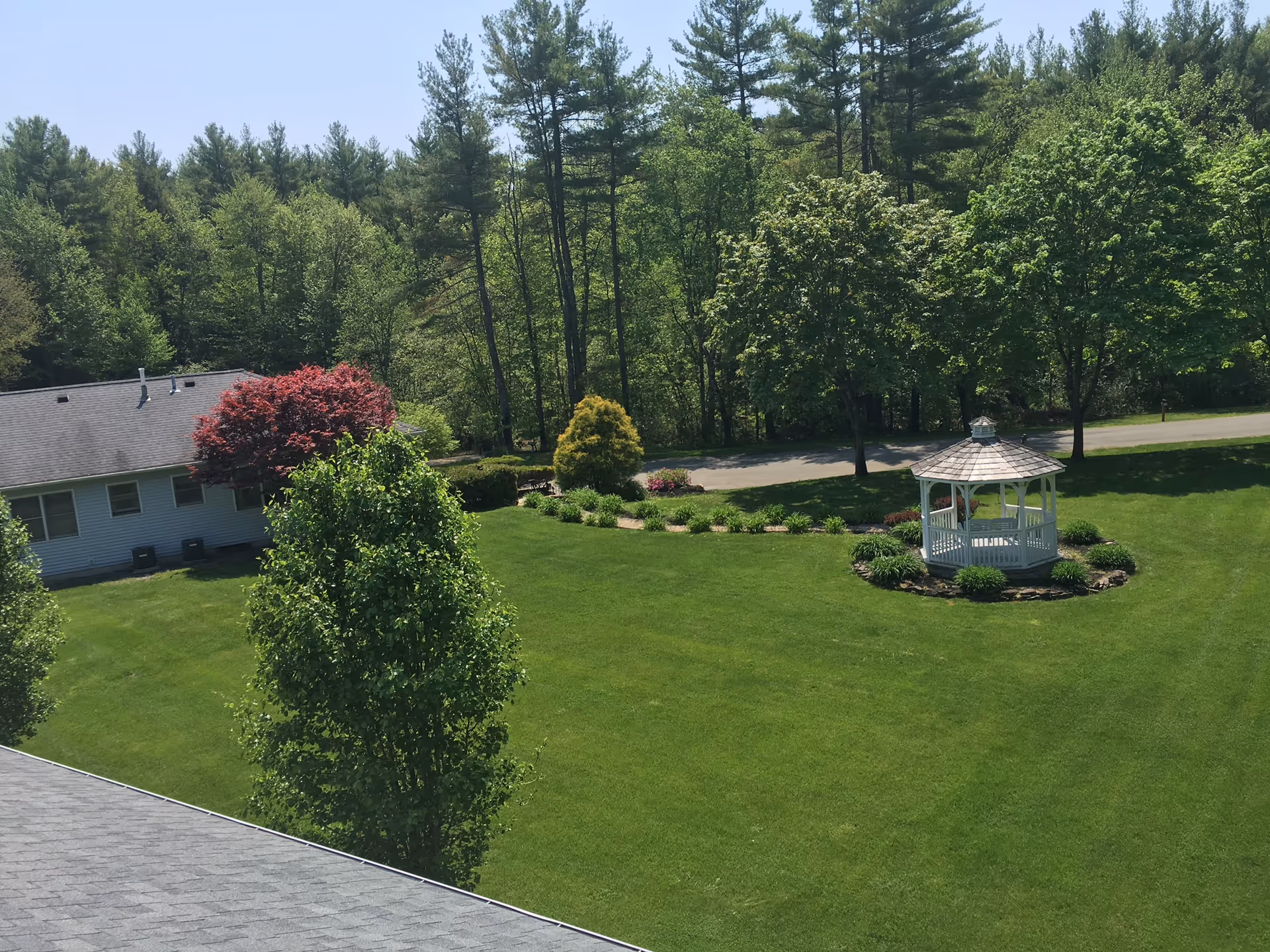A view of well-maintained green lawns and a gazebo surrounded by trees outside a residential building.
