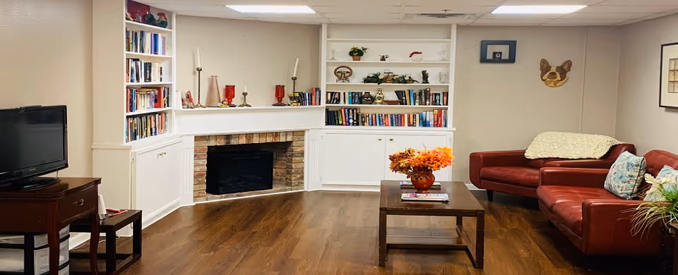 Cozy lounge with built-in white bookshelves and a fireplace, red leather sofas, a TV, and a coffee table with a floral arrangement.