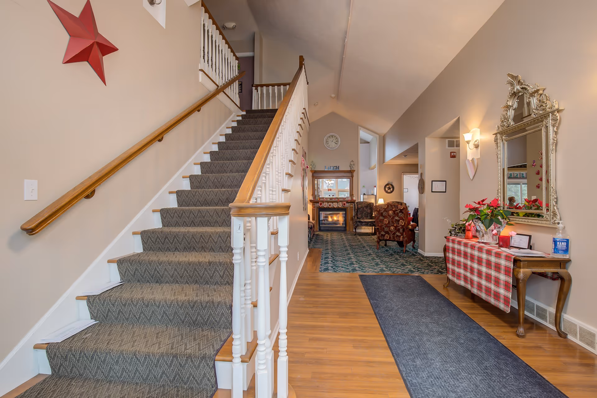 Entrance lobby with a carpeted staircase on the left, a console table and mirror on the right, and a sitting area with a fireplace in the background.