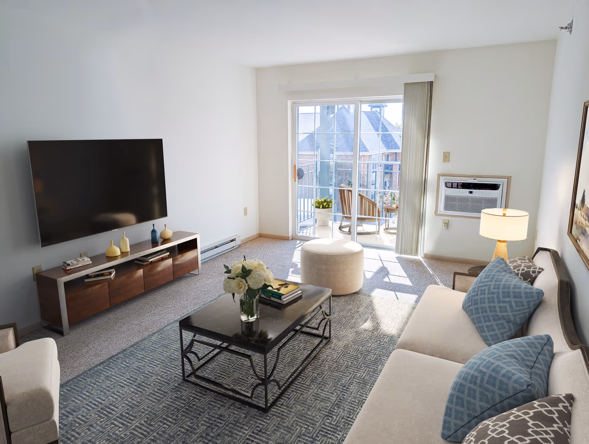 Bright living room with a sofa, coffee table, wall-mounted TV, and sliding glass door opening to a balcony.