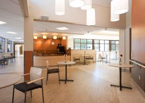 Bright interior senior living common area with round tables, chairs, and a service counter.