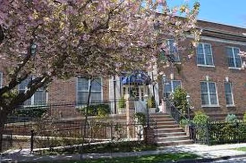 Brick senior living facility with steps, railing, and blooming tree in front
