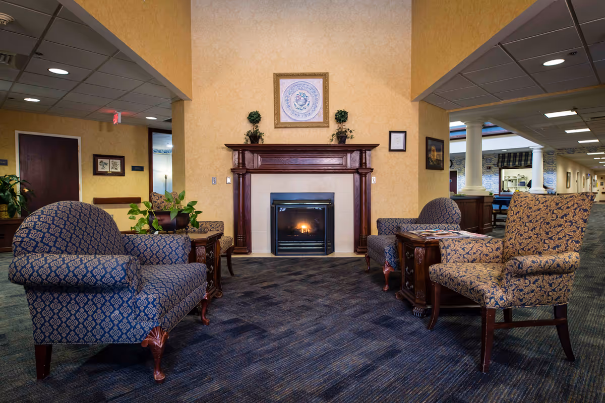 Seating area with patterned armchairs and a lit fireplace in a communal living room.
