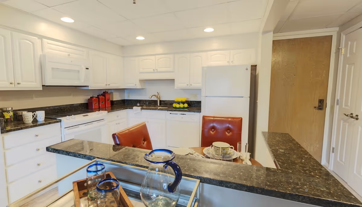 Bright kitchen with white cabinets and appliances, dark granite countertops, and a small dining counter with red chairs.