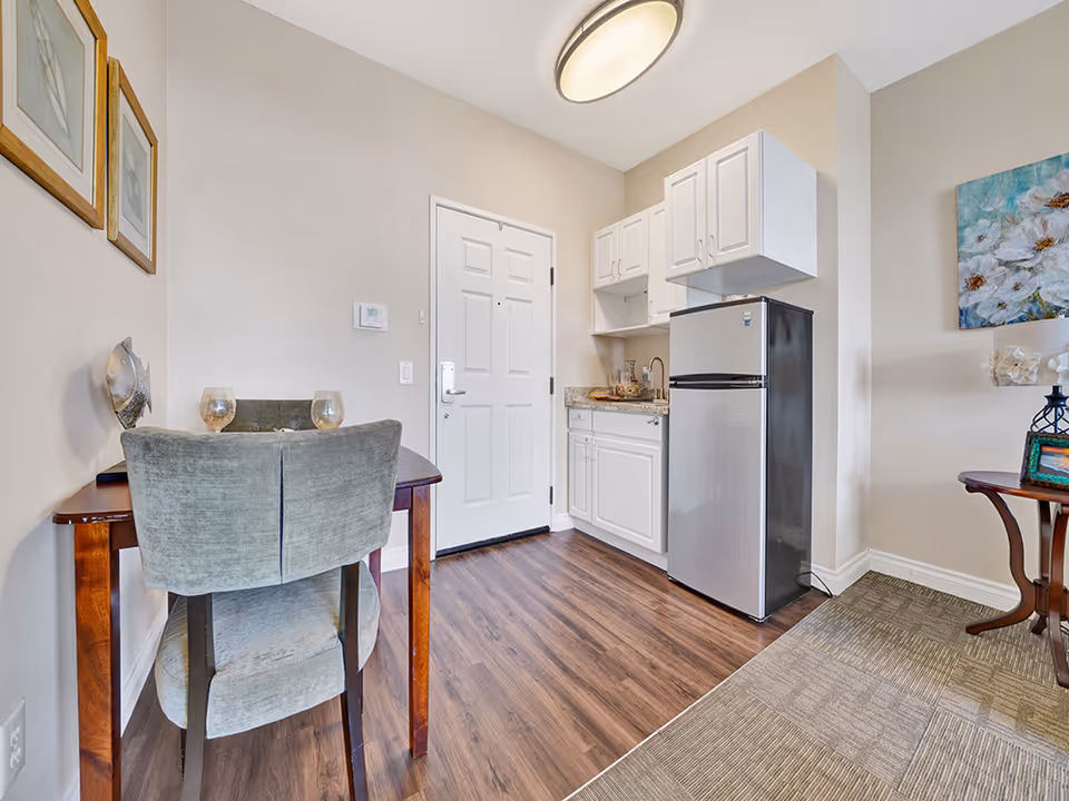 Small studio kitchenette and dining nook with a table and two chairs, white cabinets, and a stainless-steel refrigerator.