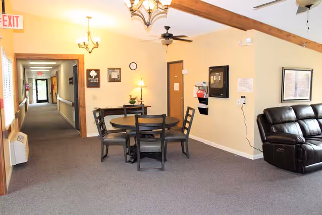 A bright common room with a round table and chairs, leather sofa, ceiling fans and a hallway leading to other rooms.