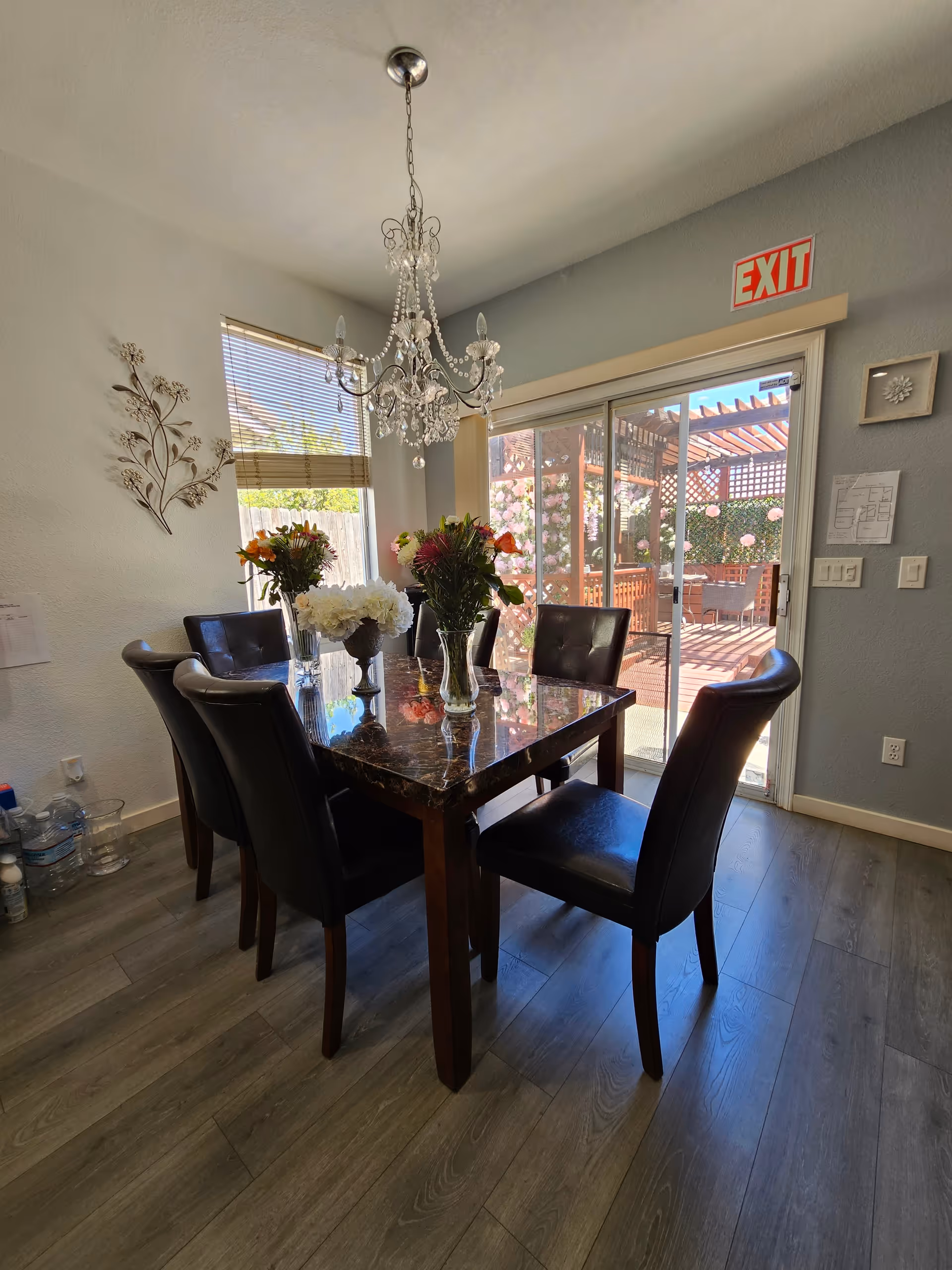 Dining room with a dark marble-top table surrounded by leather chairs, a chandelier overhead and sliding glass doors leading to a sunny patio.