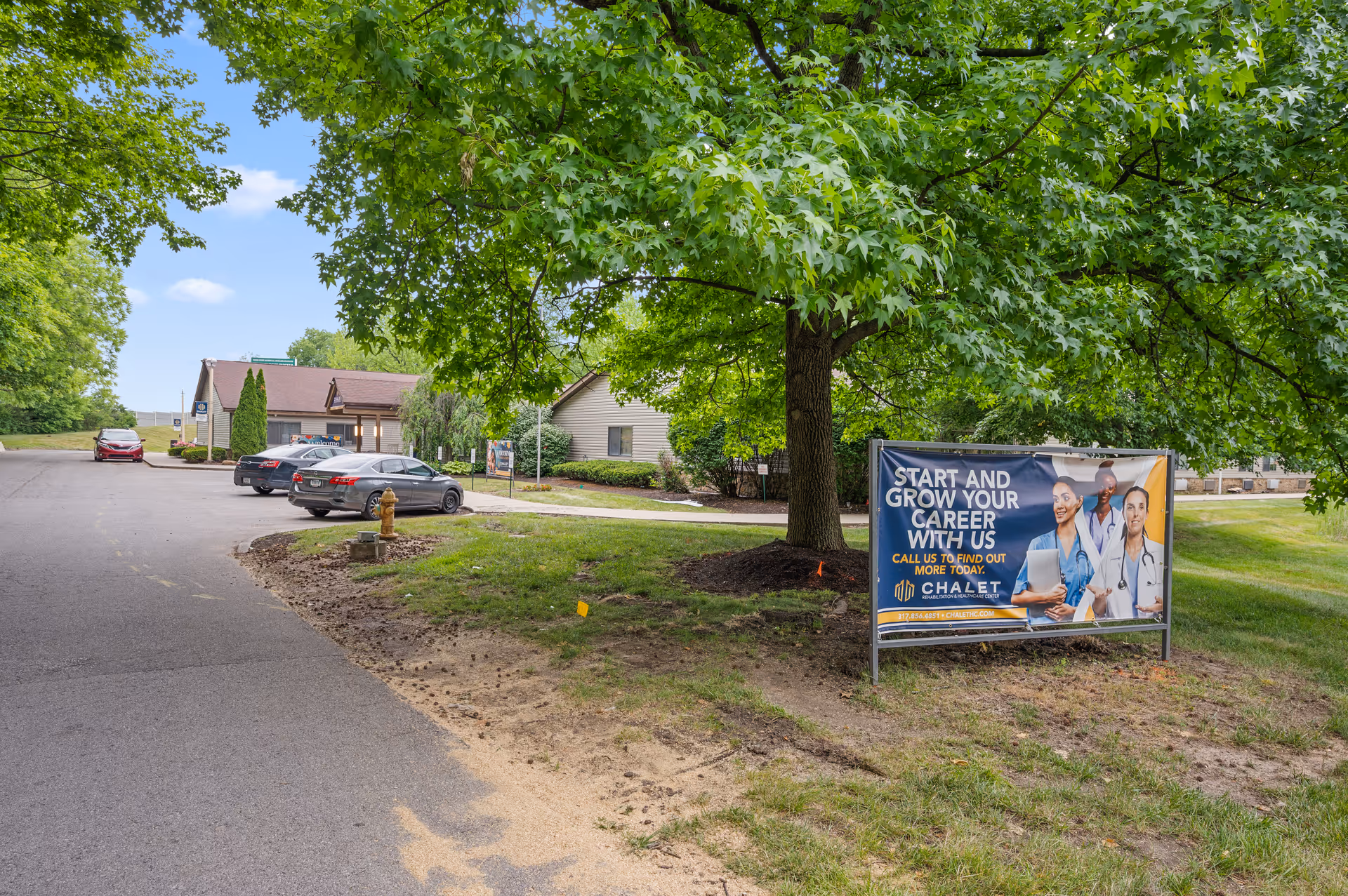 Outdoor view of Chalet Rehabilitation and Healthcare Center parking area with several parked cars, a large tree, and a recruitment banner encouraging people to start and grow their career with the facility.