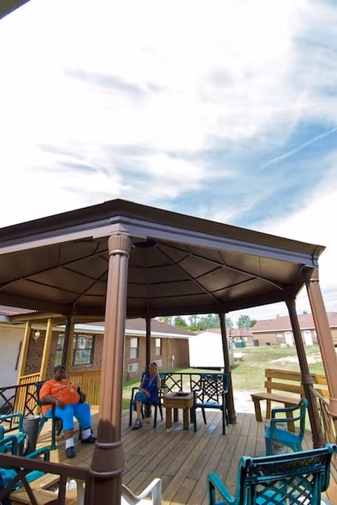Outdoor gazebo with residents seated on chairs around a wooden deck.