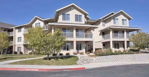 Two-story beige senior living facility with balconies and landscaped front grounds.