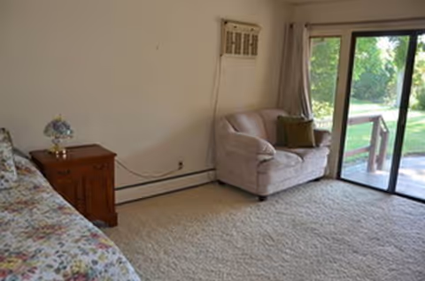 A bedroom in a senior living space with a bed, nightstand, chair, and sliding door.