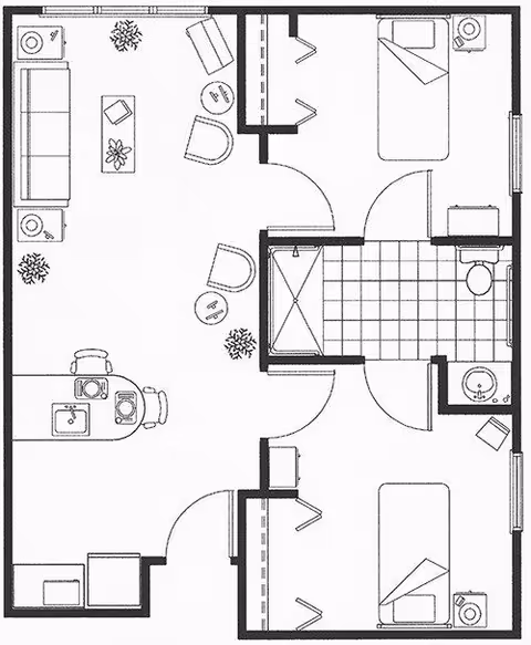 Black and white floor plan of an assisted living suite showing two bedrooms, a shared bathroom with a shower, a living area with seating and plants, and a kitchen area with a sink and dining space.