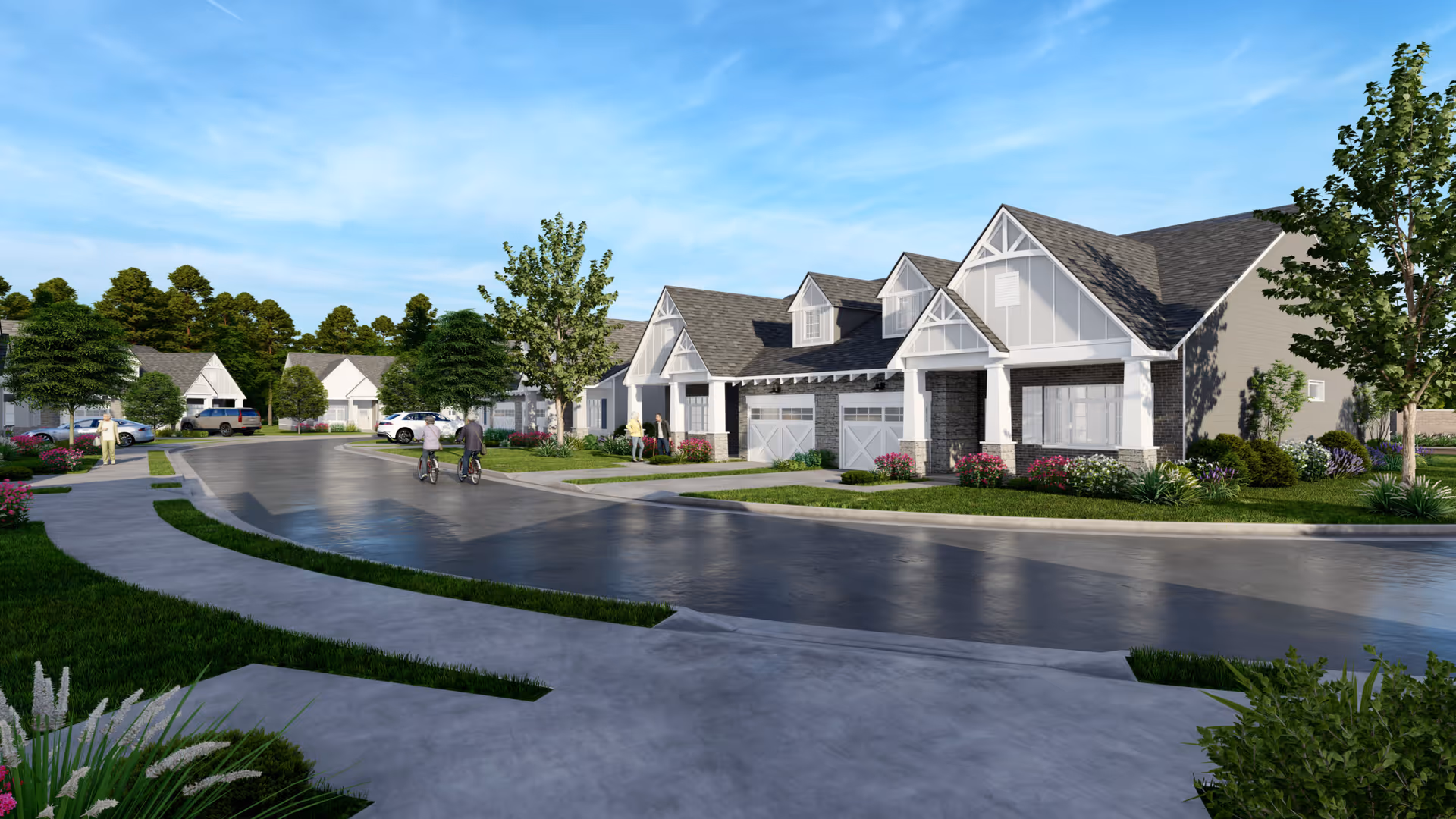 A residential community street view with single-story houses featuring gabled roofs and garages. The street is curved with sidewalks and landscaped greenery including trees, bushes, and flowers. Two people are riding bicycles on the road, and a few others are walking or standing near the houses. The sky is clear and blue.