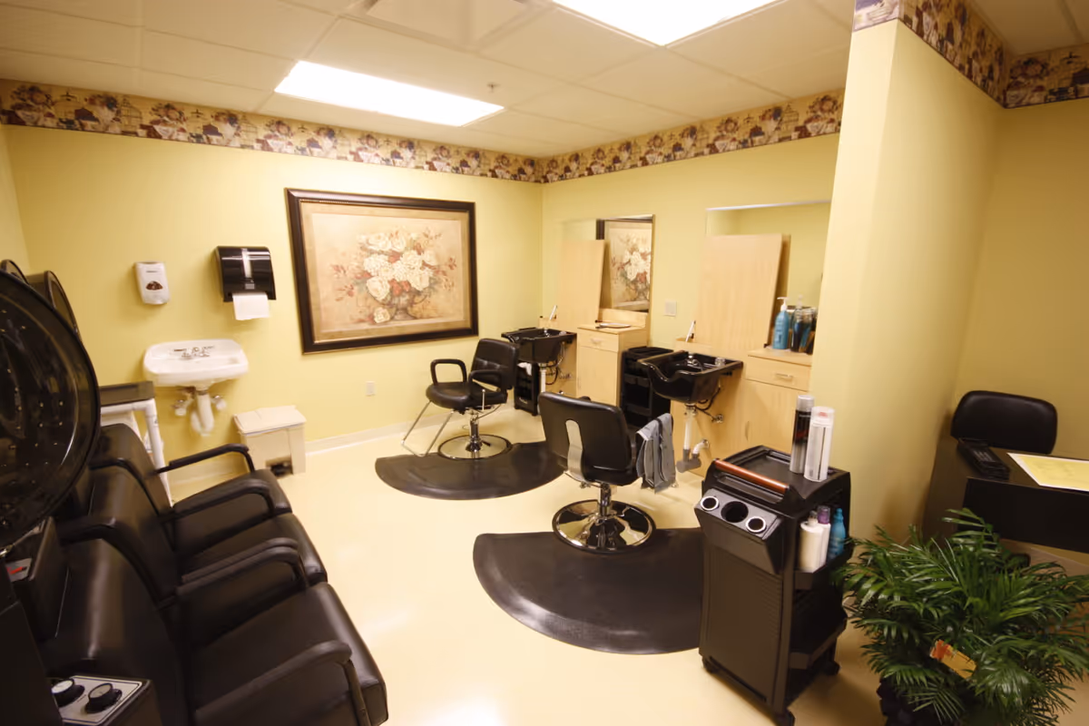 Salon-style room with styling chairs, shampoo sinks, hairdryers, and a row of waiting chairs.