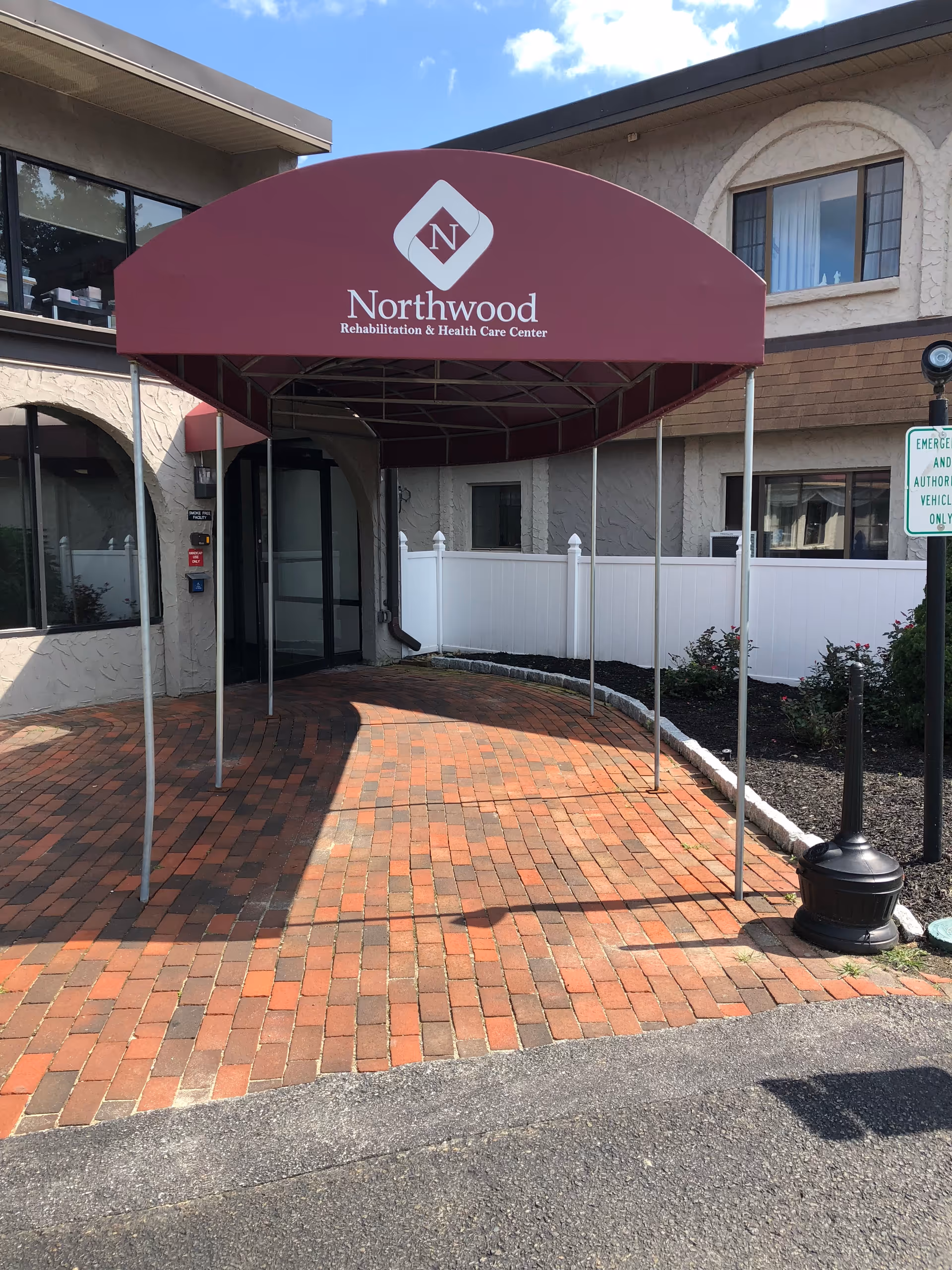 Maroon entrance canopy reading "Northwood Rehabilitation & Health Care Center" over a brick walkway leading to the facility's front doors.