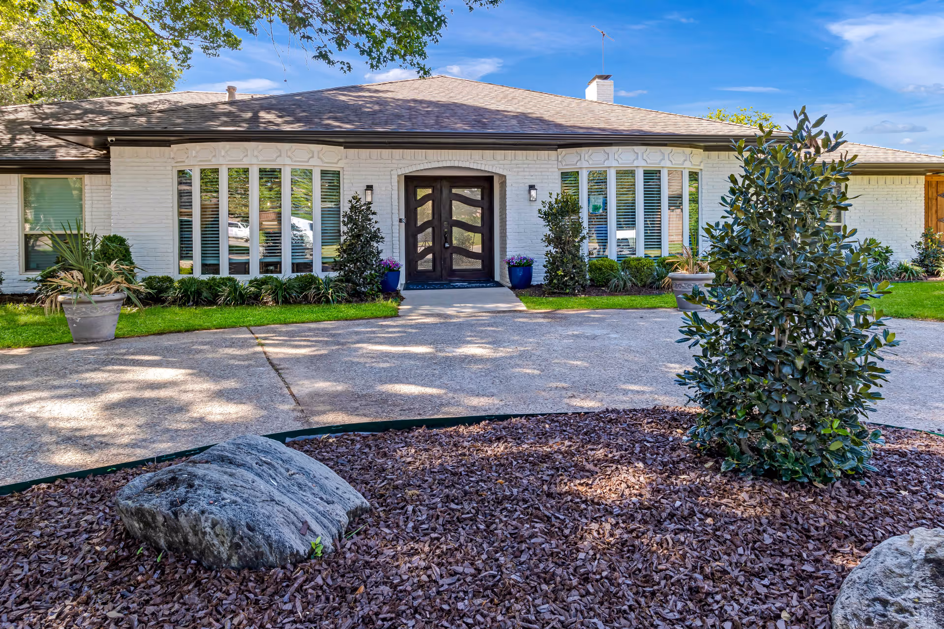 Front exterior of a single-story assisted living building with a central double-door entrance, large bay windows, and a landscaped circular driveway.