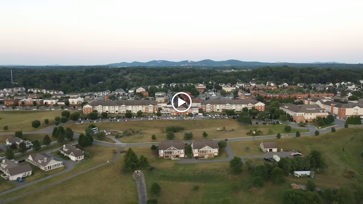 Aerial view of a senior living facility named The Summit, showing multiple buildings, parking lots, roads, and surrounding greenery with hills in the background under a clear sky.