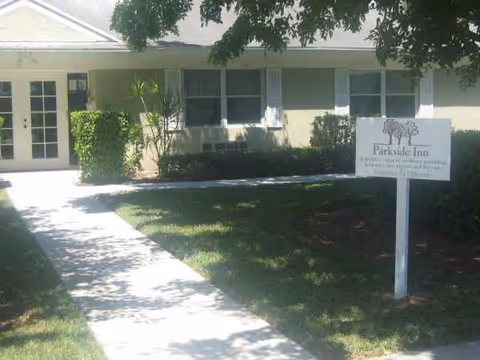 Front exterior of Parkside Inn, a single-story senior facility, with sign, walkway, and neatly trimmed lawn.
