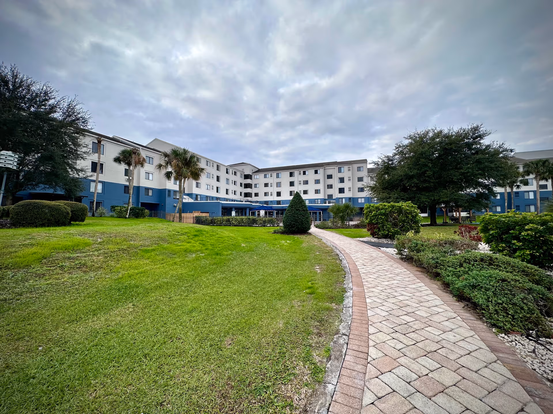 Wide view of a multi-story senior living facility with a curved brick walkway and landscaped lawn.