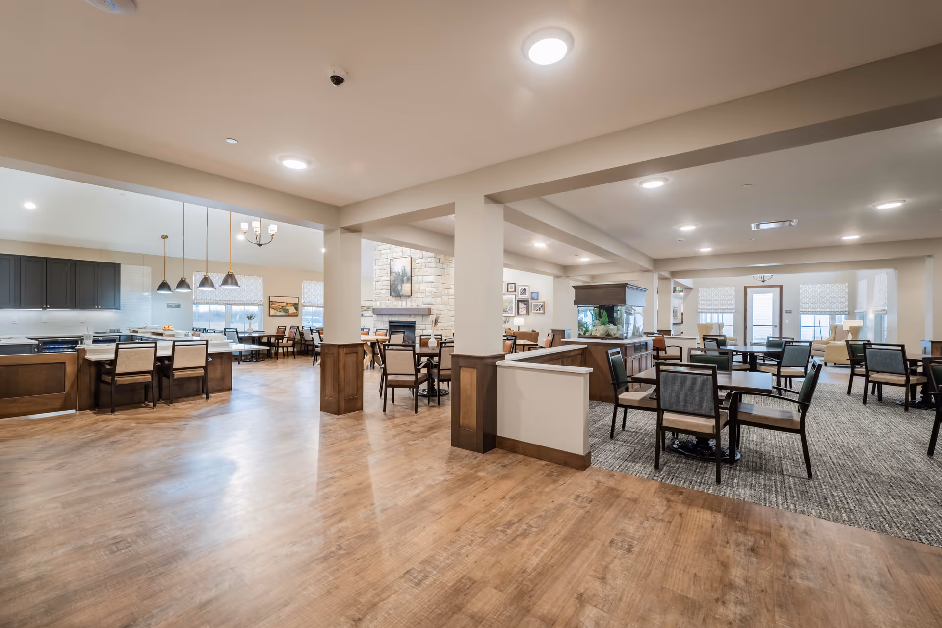 Spacious open communal dining and lounge area with a kitchen island, multiple dining tables and chairs, and a stone fireplace.