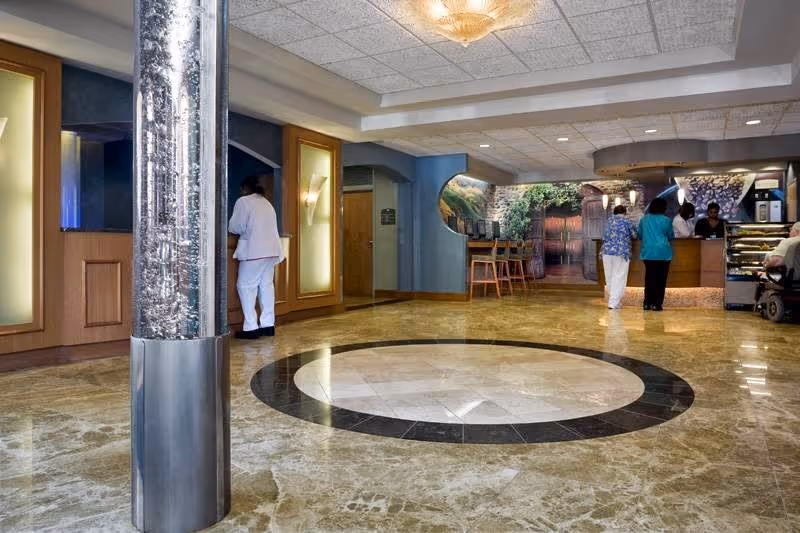 Marble-floored lobby with a circular floor inlay, decorative column, and staff and residents at a reception desk.