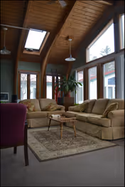 Sunlit living room with beige sectional sofas, rug, coffee table, and wooden beams.