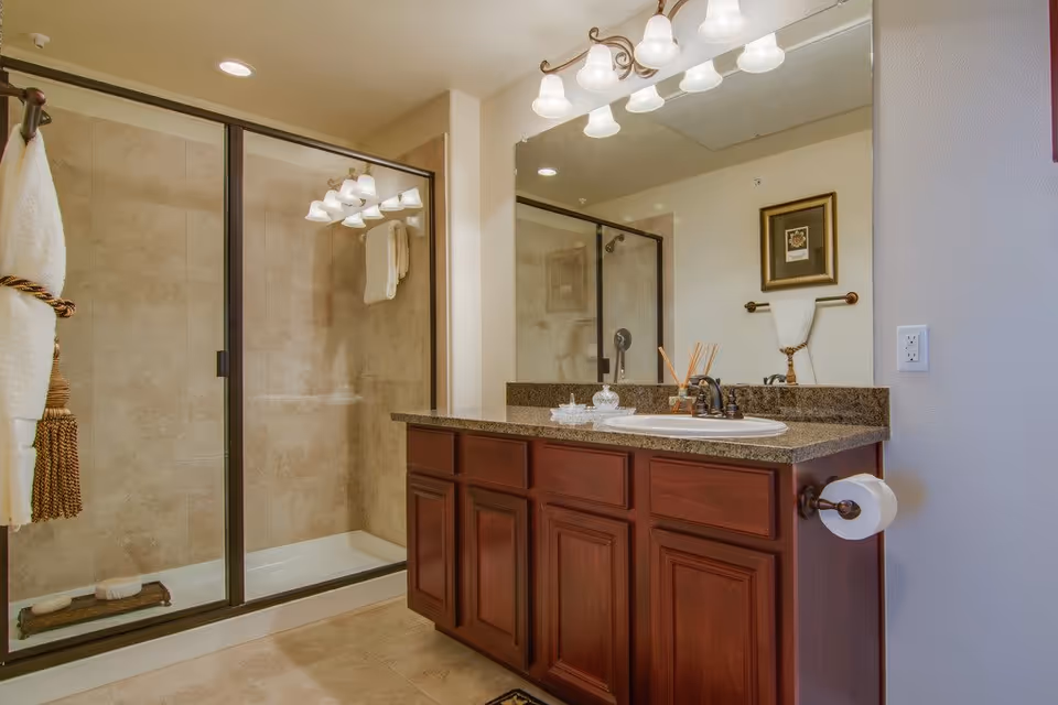 Bathroom with a wooden vanity and granite countertop, large mirror, sink, and a glass-enclosed walk-in shower.