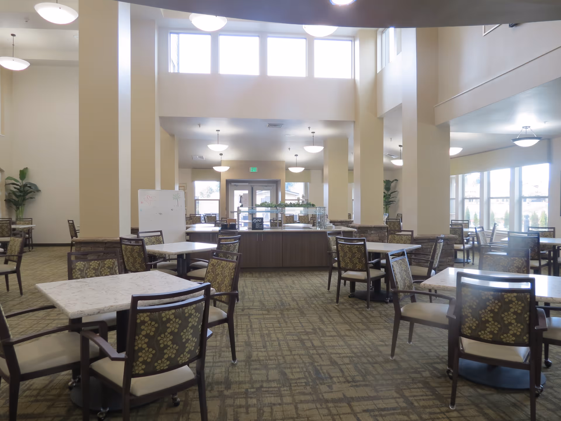 Spacious, well-lit dining room with multiple tables and chairs, high ceilings and large windows.