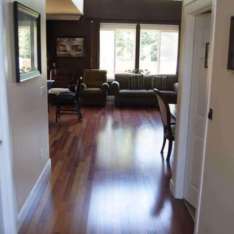Hallway view into a bright living room with leather sofas, chairs, and large windows.