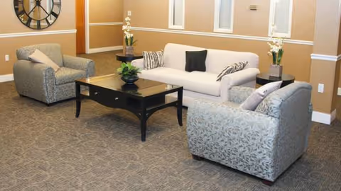 Cozy beige-walled lounge with white sofa, patterned chairs, and a glass-top coffee table.