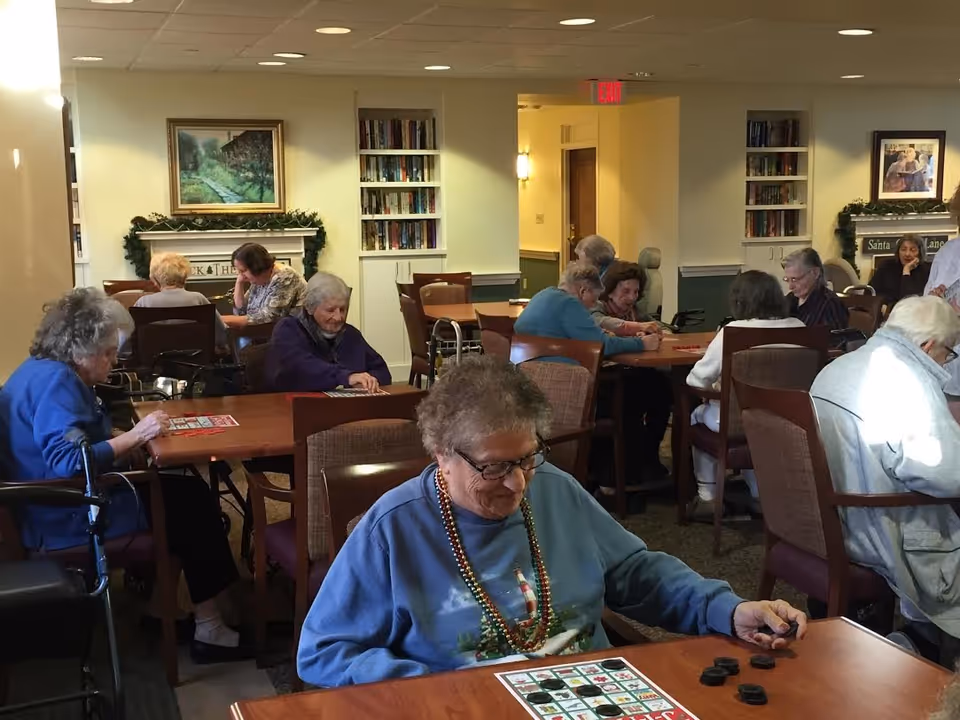 Several elderly residents seated at tables in a communal room playing bingo and card games.