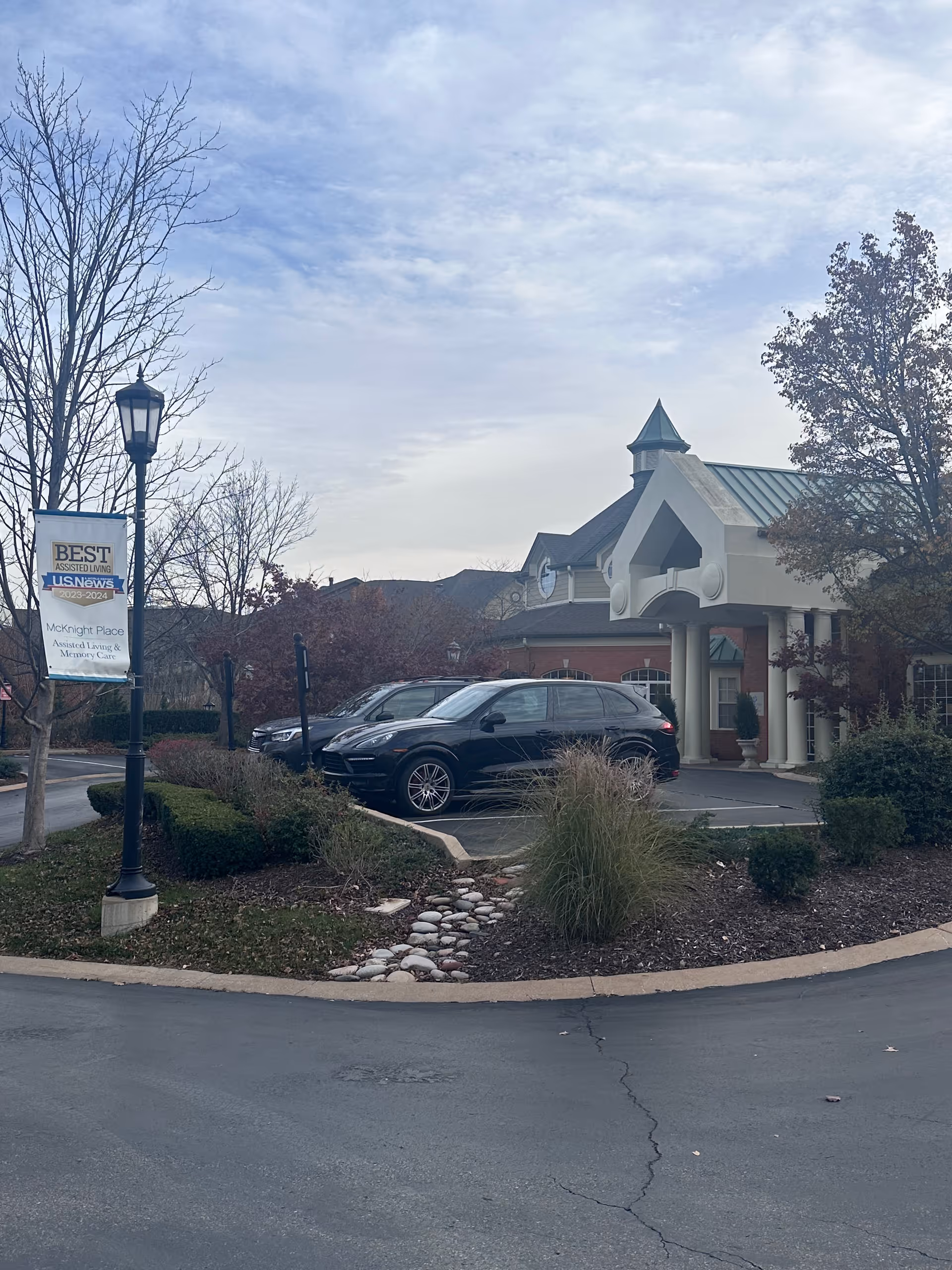 Entrance and front exterior of McKnight Place assisted living facility with parked cars, landscaping, and a lamppost sign.