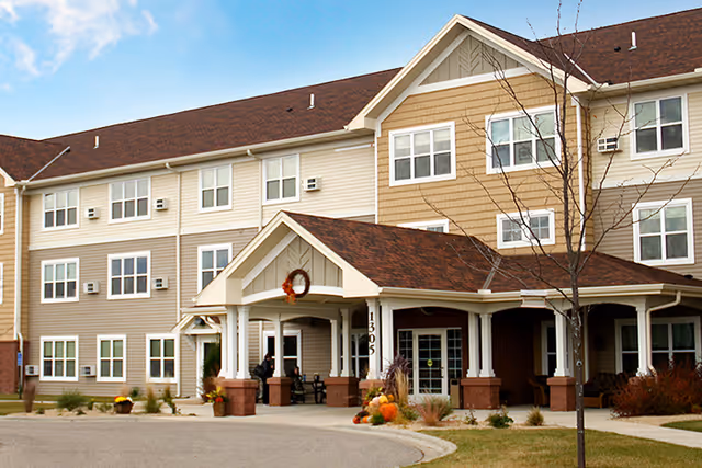 Exterior view of a senior living facility with a covered entrance and pumpkins outside.
