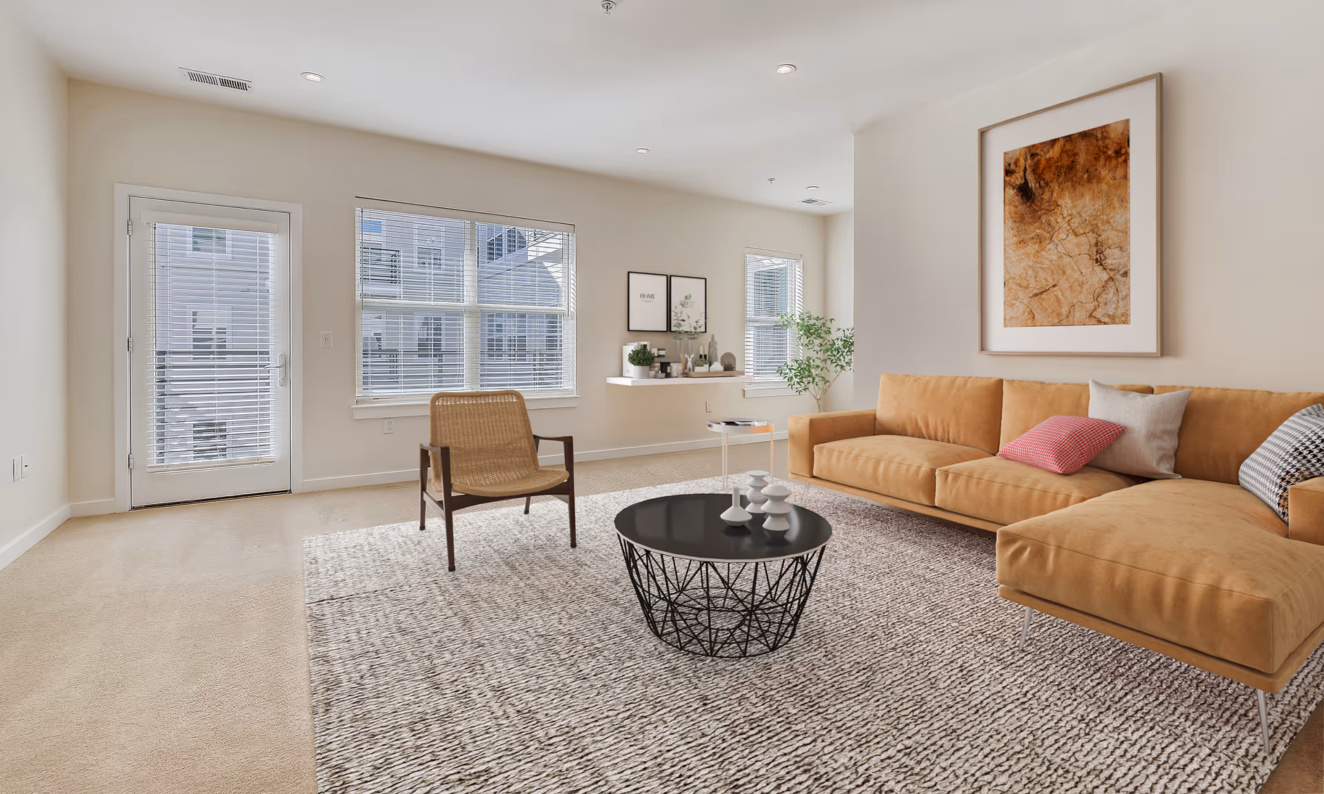 Bright living room with a tan sectional sofa, woven chair, round black coffee table, and large windows with a door to a balcony.