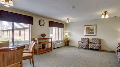 Cozy senior living lounge with fireplace, window seating, and patterned chairs.