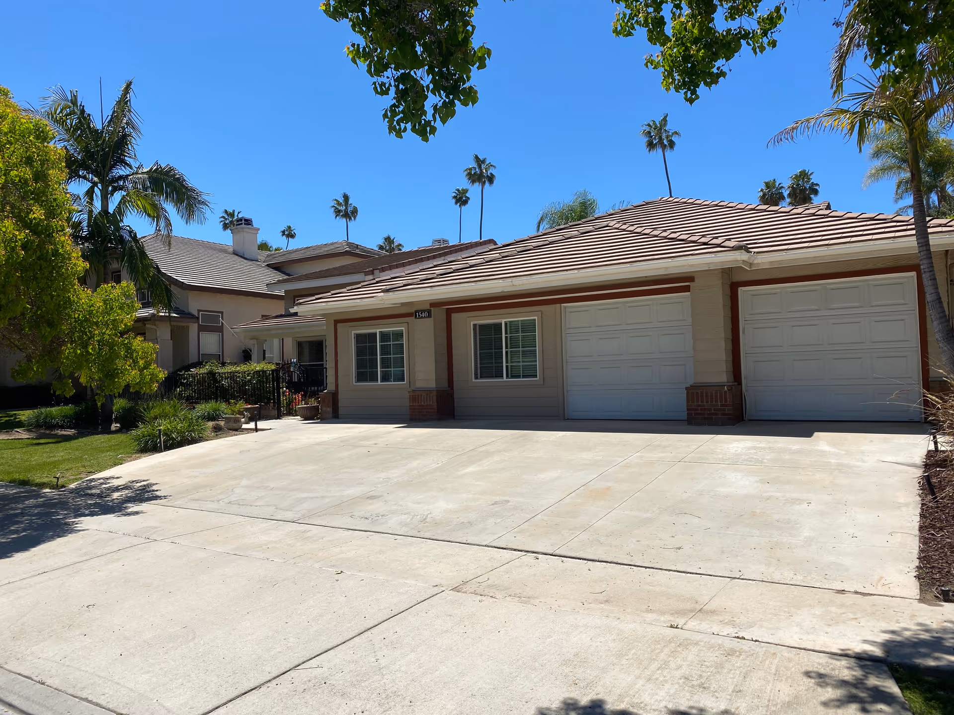 Residential-style senior living facility front with two garage doors, driveway, and palm trees.