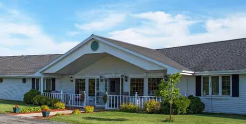 Front view of a single-story senior living facility with a porch and landscaped lawn.